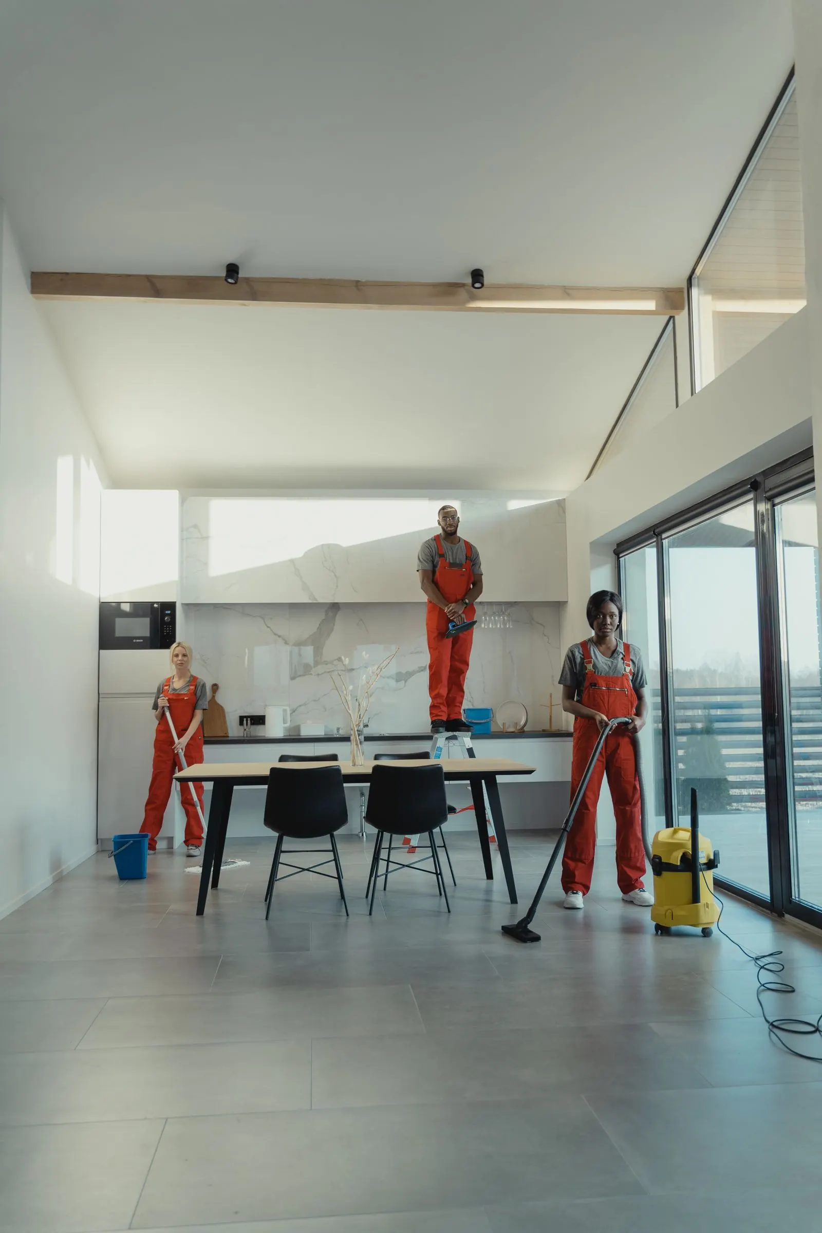 Cleaning crew in uniforms mopping, dusting, and vacuuming a bright, open office space