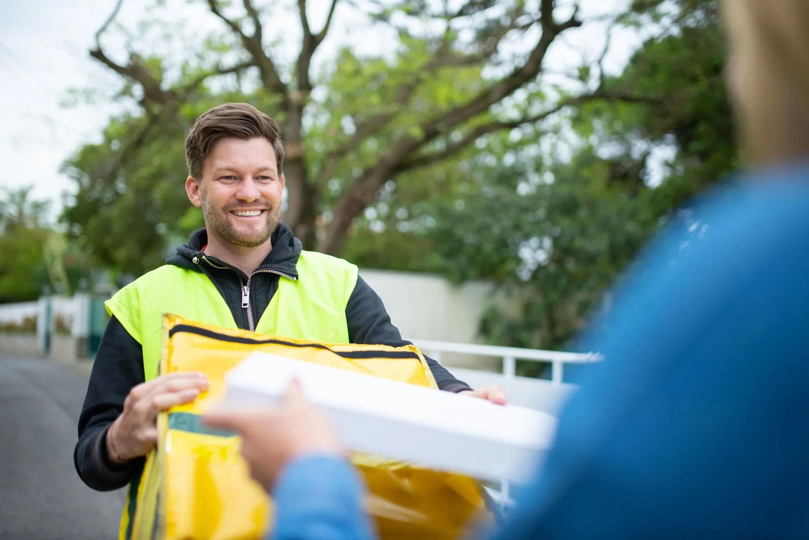 Smiling delivery worker in a safety vest handing over a package