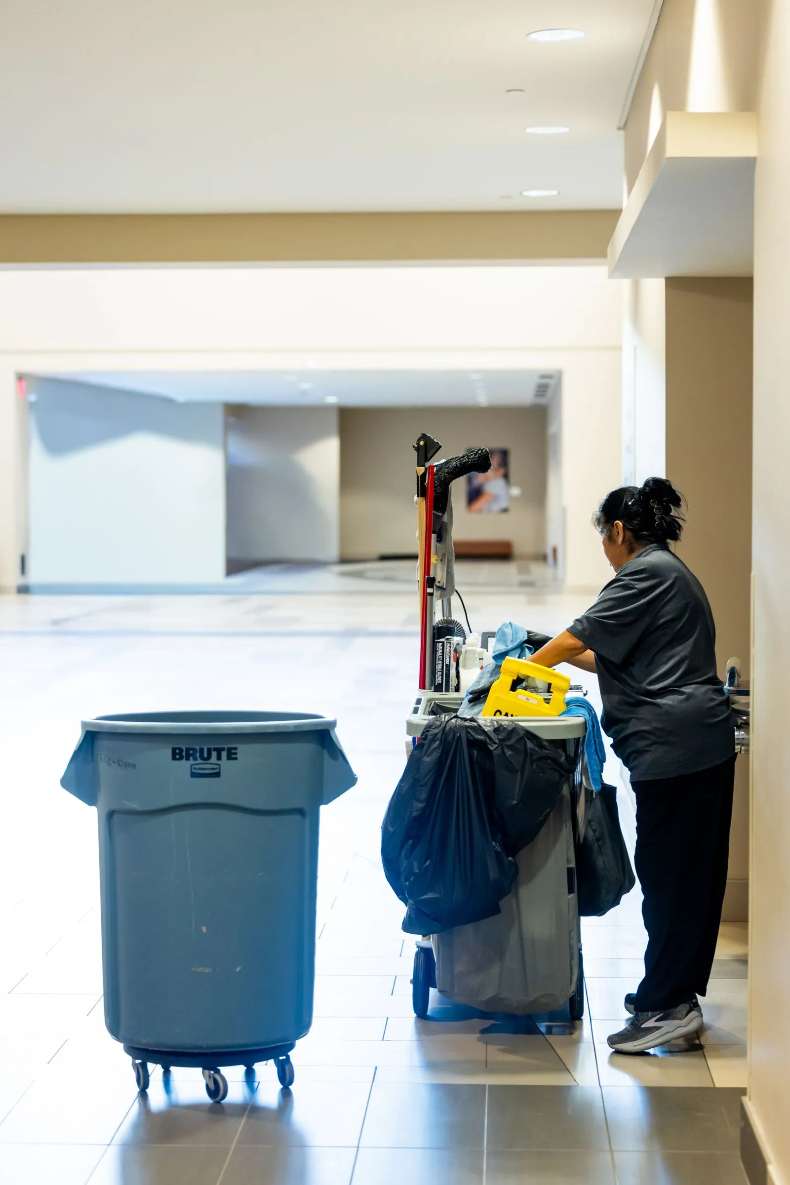 Janitorial worker with a cleaning cart in a bright, spotless hallway