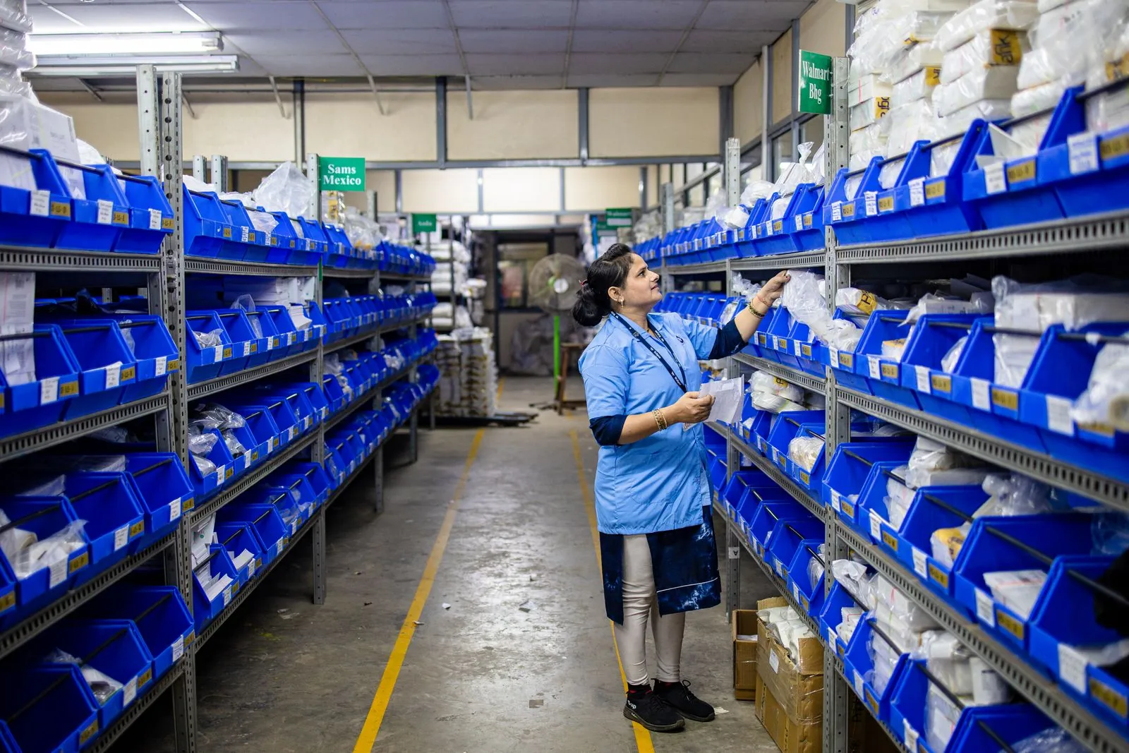 Warehouse worker organizing supplies on shelves of blue bins